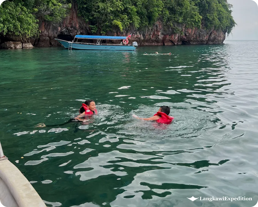 Tourists swimming in emerald waters near a limestone island in Langkawi